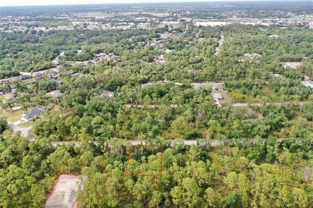 An aerial view shows a wooded residential lot outlined in red amidst a suburban neighborhood — 14051 STANFIELD AVENUE, PORT CHARLOTTE, FL