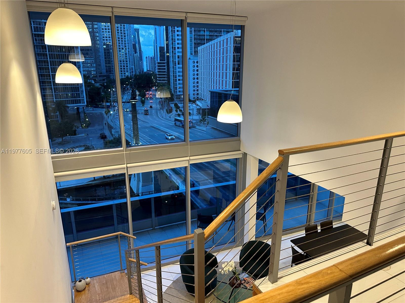 A high-ceilinged room features floor-to-ceiling windows overlooking a city street and a staircase — 200 S Biscayne Boulevard Way # 703, Miami FL 33131, MIAMI, FL