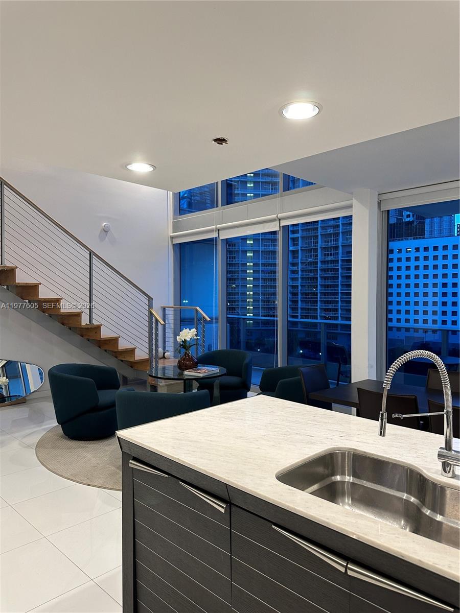 A modern kitchen island overlooks a living area with a staircase and floor-to-ceiling windows — 200 S Biscayne Boulevard Way # 703, Miami FL 33131, MIAMI, FL