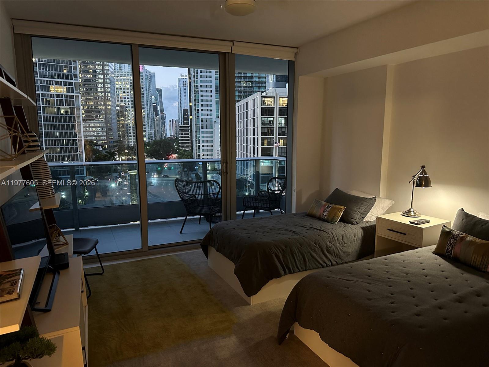 A bedroom with two twin beds, a nightstand, and a balcony overlooking city skyscrapers — 200 S Biscayne Boulevard Way # 703, Miami FL 33131, MIAMI, FL