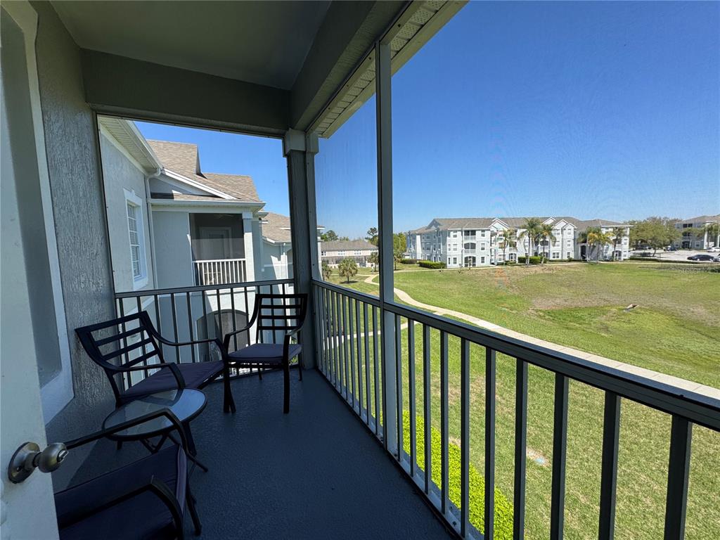 A screened-in balcony features metal railings, patio furniture, and a view of a grassy field — 2305 SILVER PALM DRIVE UNIT 302, KISSIMMEE, FL