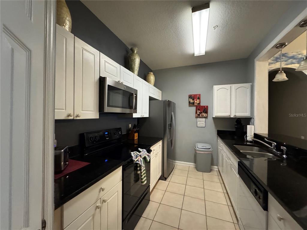 A galley kitchen features white cabinets, black countertops, stainless steel appliances, and tiled flooring — 2305 SILVER PALM DRIVE UNIT 302, KISSIMMEE, FL