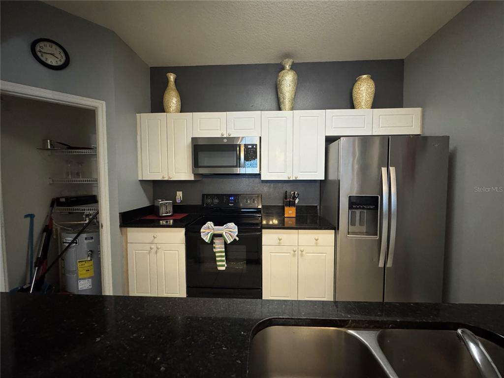 A kitchen features white cabinets, black countertops, a black stove, and a stainless steel refrigerator — 2305 SILVER PALM DRIVE UNIT 302, KISSIMMEE, FL