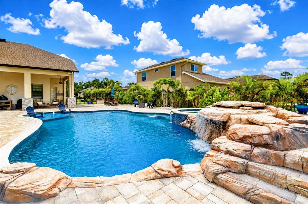 A backyard swimming pool features a rock waterfall, a sun shelf, and a paved patio — 9451 59TH STREET N, PINELLAS PARK, FL
