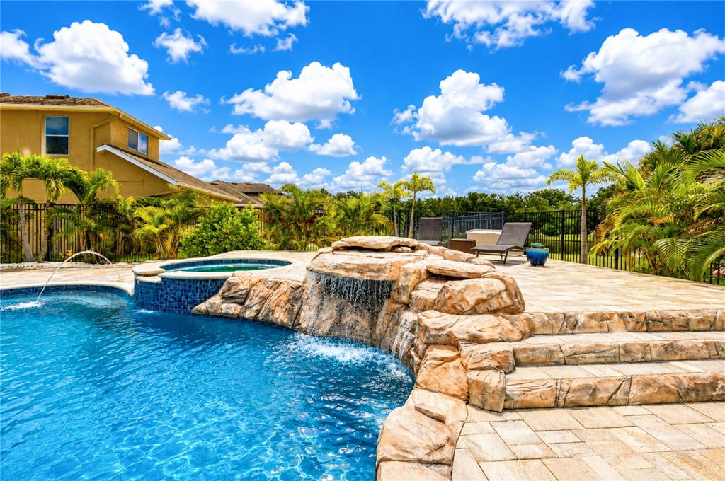 A backyard swimming pool features a rock waterfall, a raised spa, and a stone patio — 9451 59TH STREET N, PINELLAS PARK, FL