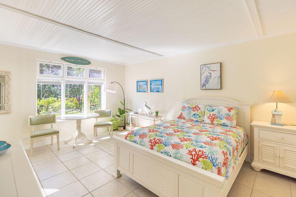 A bedroom with a coral-patterned bed, white furniture, tile floors, and a small dining table — 88 S Ocean Boulevard, Delray Beach FL 33483, DELRAY BEACH, FL