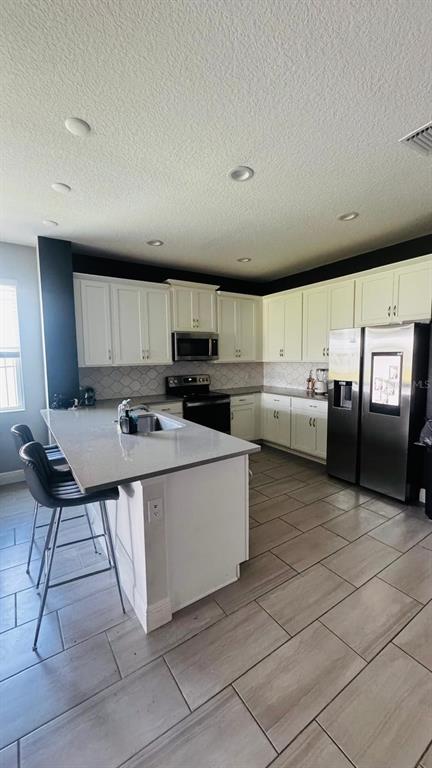 A kitchen features white cabinets, a quartz island with bar seating, and light tile flooring — 2695 NOTTEL DRIVE, ST CLOUD, FL