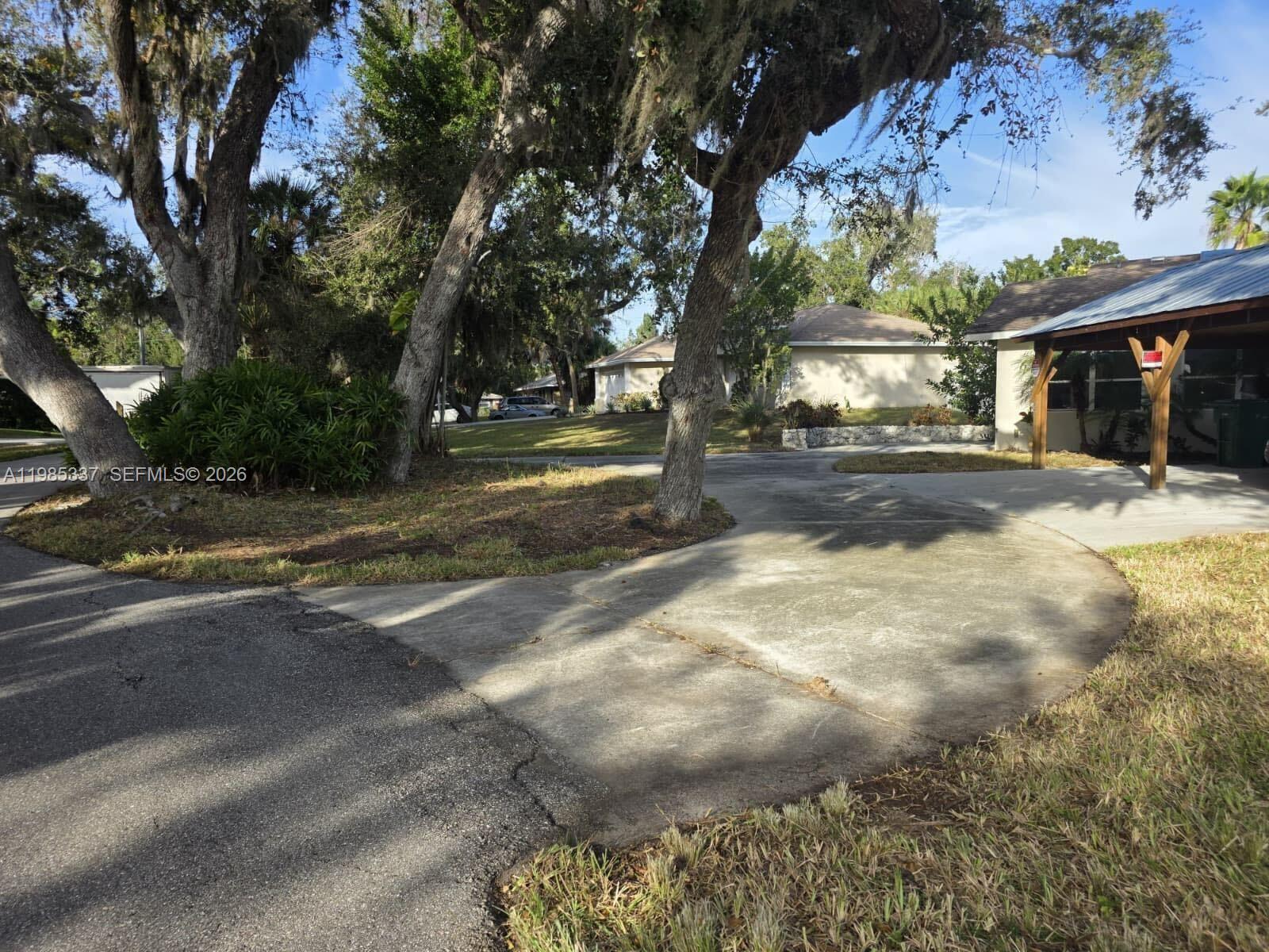 A concrete driveway leads to a house with a covered porch under large oak trees — 3661 Bernice LN, Sarasota FL 34238, SARASOTA, FL