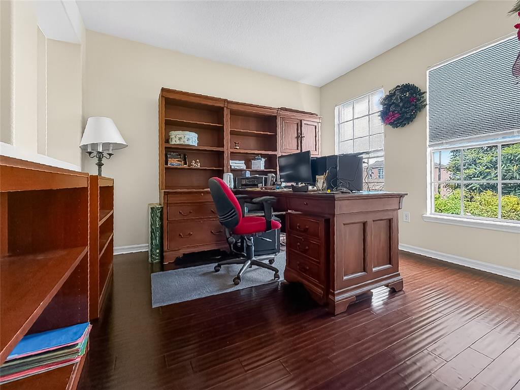 A home office features dark wood flooring, a large wooden desk, and built-in shelving — 25143 CHIPSHOT COURT, SORRENTO, FL