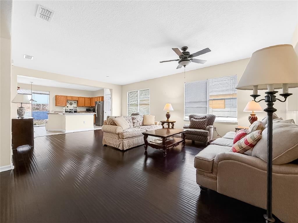 A spacious living room with dark hardwood floors, beige furniture, and an open kitchen beyond — 25143 CHIPSHOT COURT, SORRENTO, FL