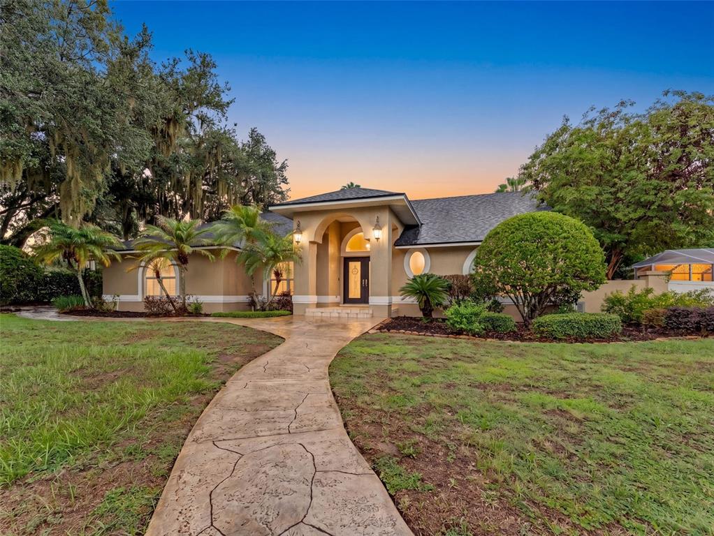 A single-story house with a tan stucco exterior, arched entryway, and a stone walkway — 6626 CRESCENT LAKE DRIVE, LAKELAND, FL