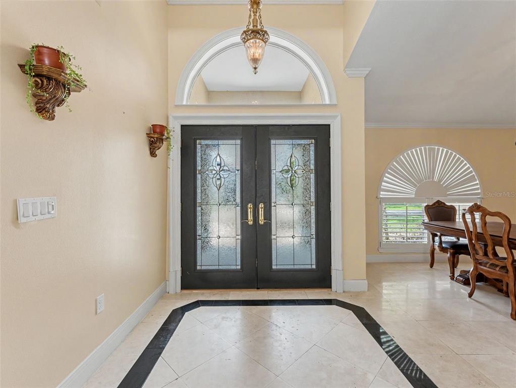 An entryway features double glass-paneled doors, a tiled floor with a black border, and wall sconces — 6626 CRESCENT LAKE DRIVE, LAKELAND, FL