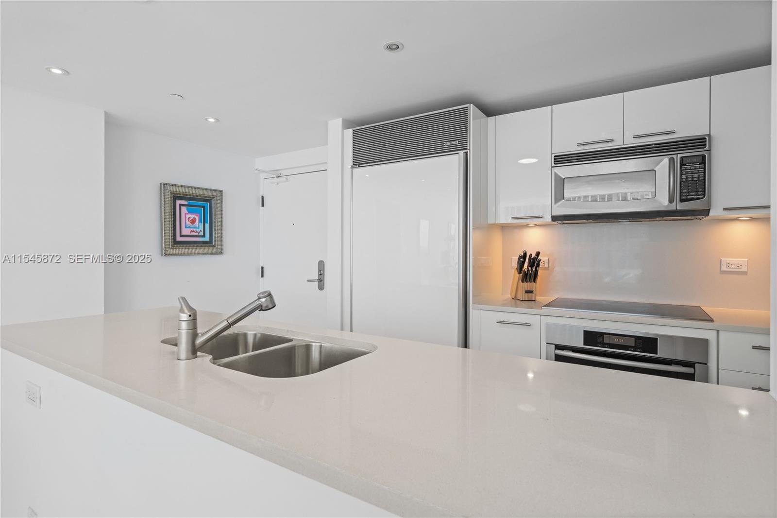 A modern kitchen features white cabinetry, stainless steel appliances, and a quartz-topped island with sink — 6801 Collins Ave # 1206, Miami Beach FL 33141, MIAMI BEACH, FL