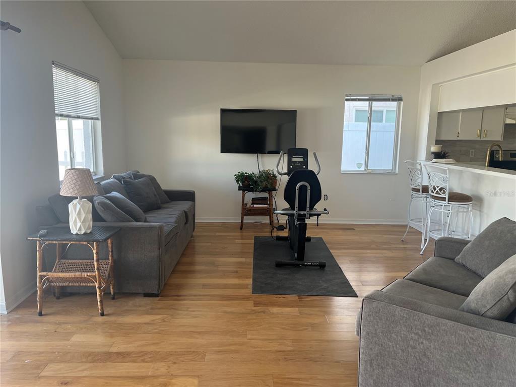 A living room features hardwood floors, two gray sofas, a wall-mounted television, and an exercise bike — 2930 SHANNON CIR, PALM HARBOR, FL