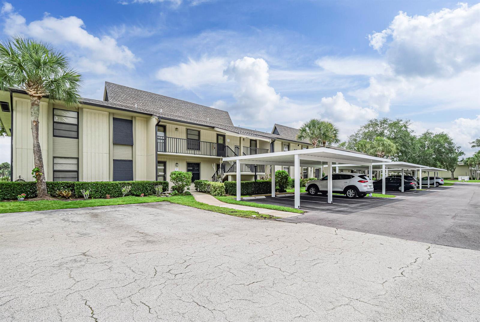 An exterior view of a two-story apartment building with covered parking and palm trees — 23 Plantation Drive # 102, Vero Beach FL 32966, VERO BEACH, FL