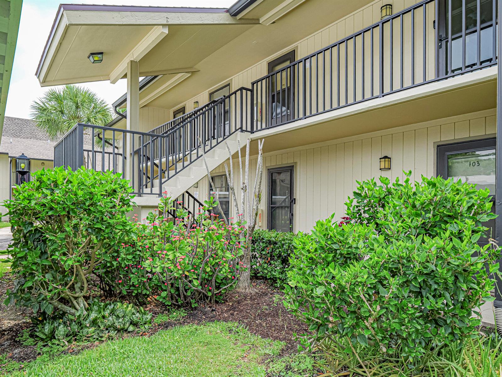 Exterior view of a two-story apartment building with a staircase and lush landscaping — 23 Plantation Drive # 102, Vero Beach FL 32966, VERO BEACH, FL