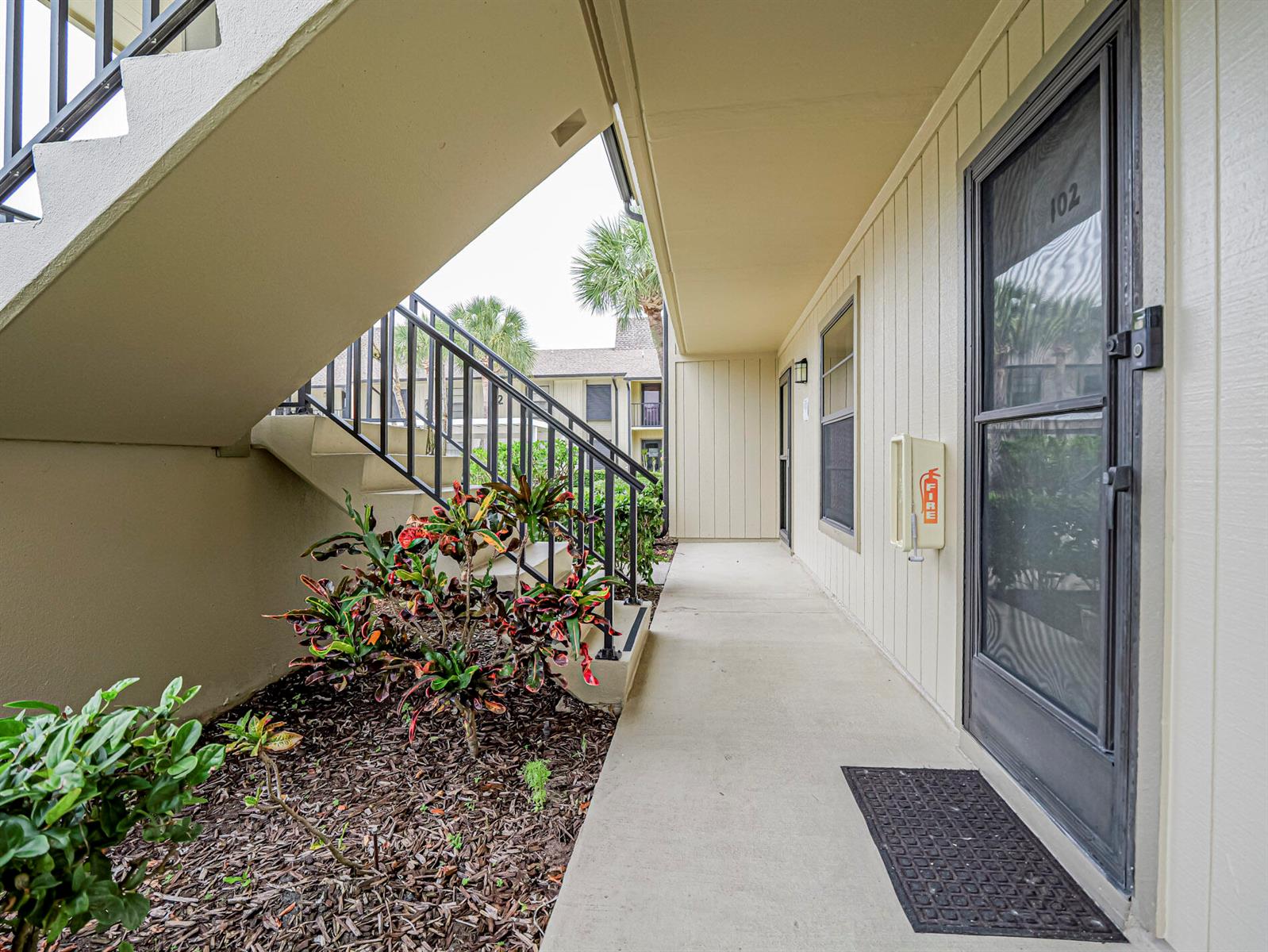 An exterior walkway leads to a ground-floor apartment entrance with a fire extinguisher cabinet — 23 Plantation Drive # 102, Vero Beach FL 32966, VERO BEACH, FL