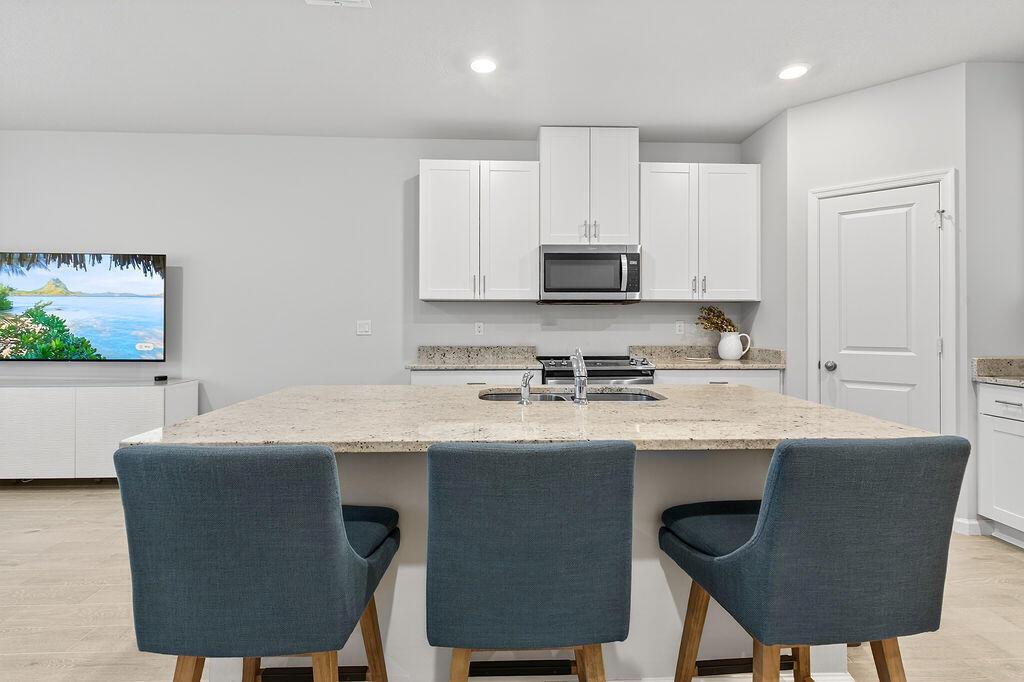 A kitchen features a large granite island with three blue chairs and white cabinetry — 5696 SE Edgewater Circle, Stuart FL 34997, STUART, FL
