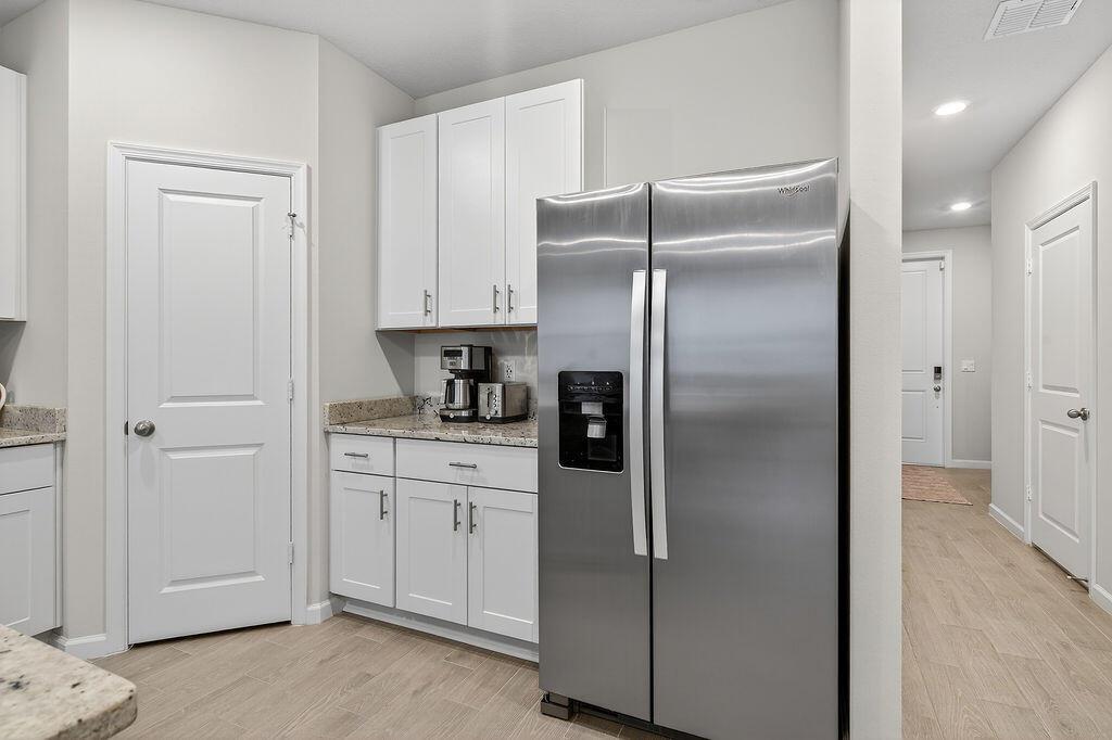 A kitchen features white cabinets, granite countertops, a stainless steel refrigerator, and light wood flooring — 5696 SE Edgewater Circle, Stuart FL 34997, STUART, FL