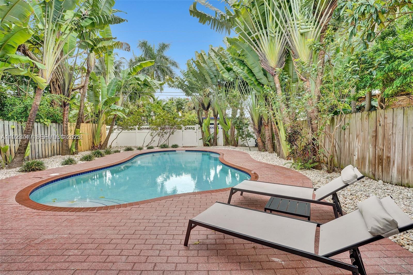 A backyard swimming pool features a brick patio and lounge chairs surrounded by tropical landscaping — 1640 Jefferson St, Hollywood FL 33020, HOLLYWOOD, FL
