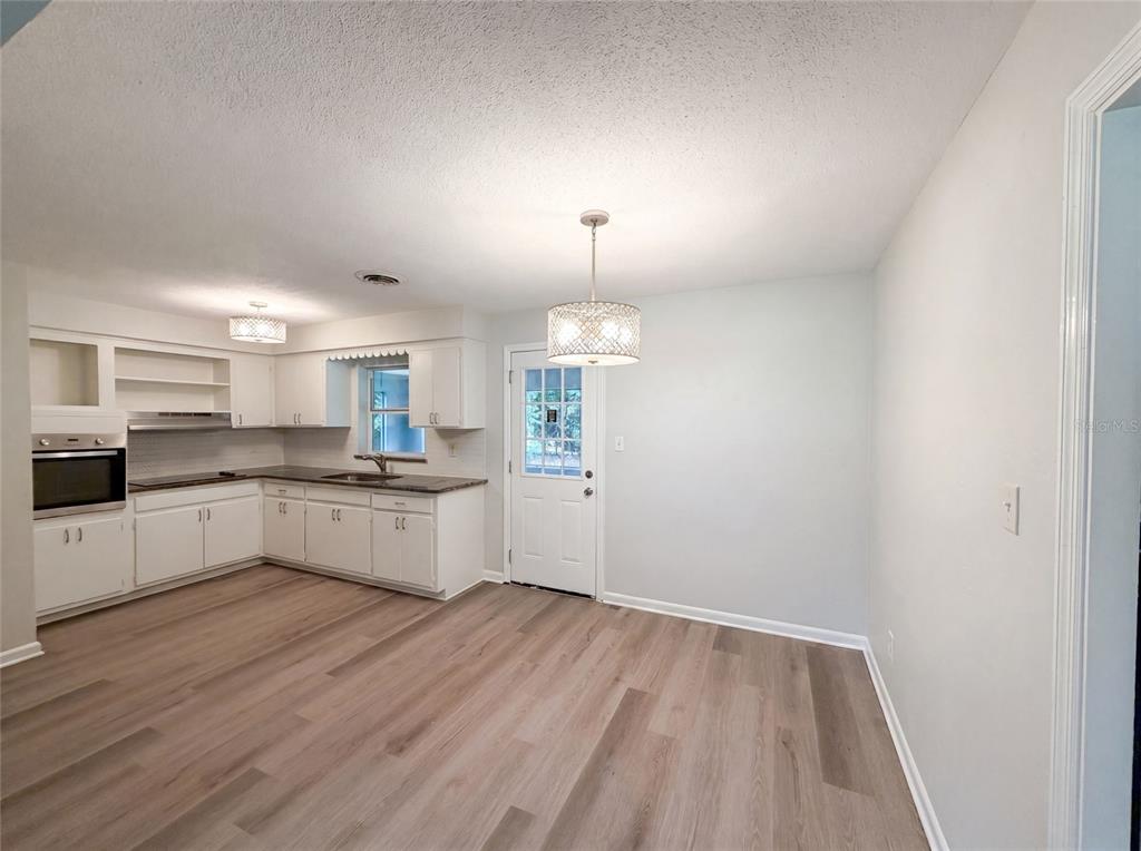 A kitchen and dining area with white cabinets, dark countertops, and light wood-look flooring — 2410 NE 3RD AVENUE, OCALA, FL