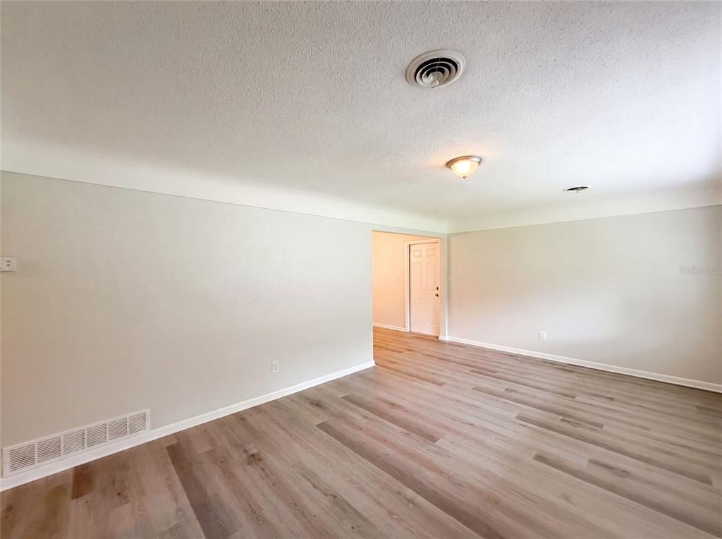 An empty room features light-colored wood-look flooring, white walls, and a ceiling light fixture — 2410 NE 3RD AVENUE, OCALA, FL