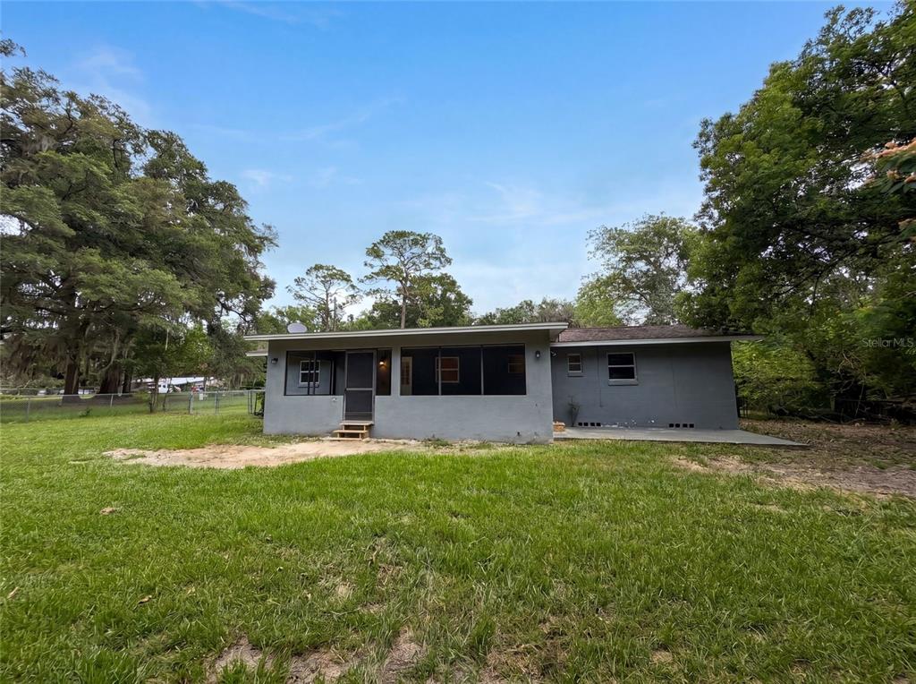 The back exterior of a gray house features a screened porch and a concrete patio — 2410 NE 3RD AVENUE, OCALA, FL