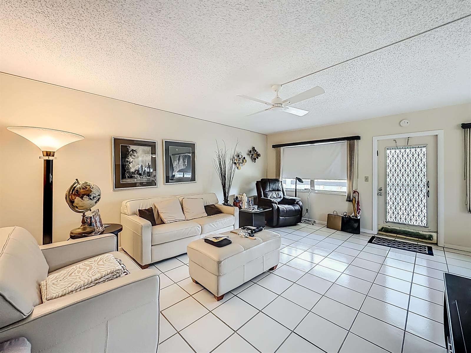A living room features white tile flooring, a beige sofa, a matching ottoman, and a ceiling fan — 2114 Oakridge V, Deerfield Beach FL 33442, DEERFIELD BEACH, FL