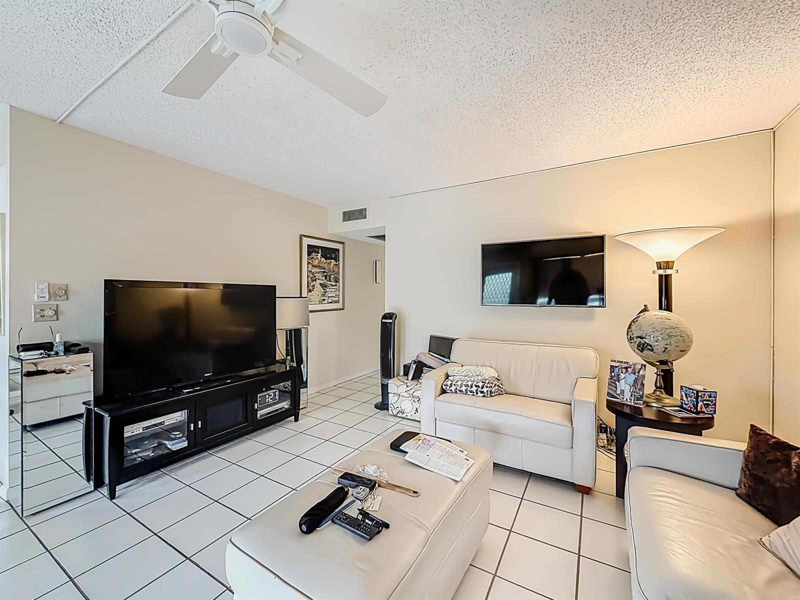 A living room features white tile flooring, a ceiling fan, two white sofas, and televisions — 2114 Oakridge V, Deerfield Beach FL 33442, DEERFIELD BEACH, FL