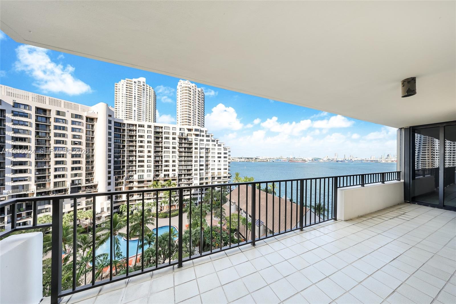 A balcony with white tile flooring overlooks a swimming pool, nearby high-rise buildings, and water — 520 Brickell Key Dr # A1104, Miami FL 33131, MIAMI, FL