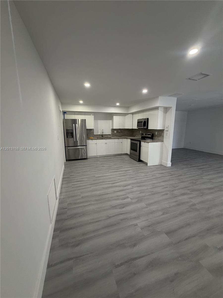 A modern kitchen features white cabinets, stainless steel appliances, and light gray wood-look flooring — 9401 SW 64th Ter # 0, Miami FL 33173, MIAMI, FL
