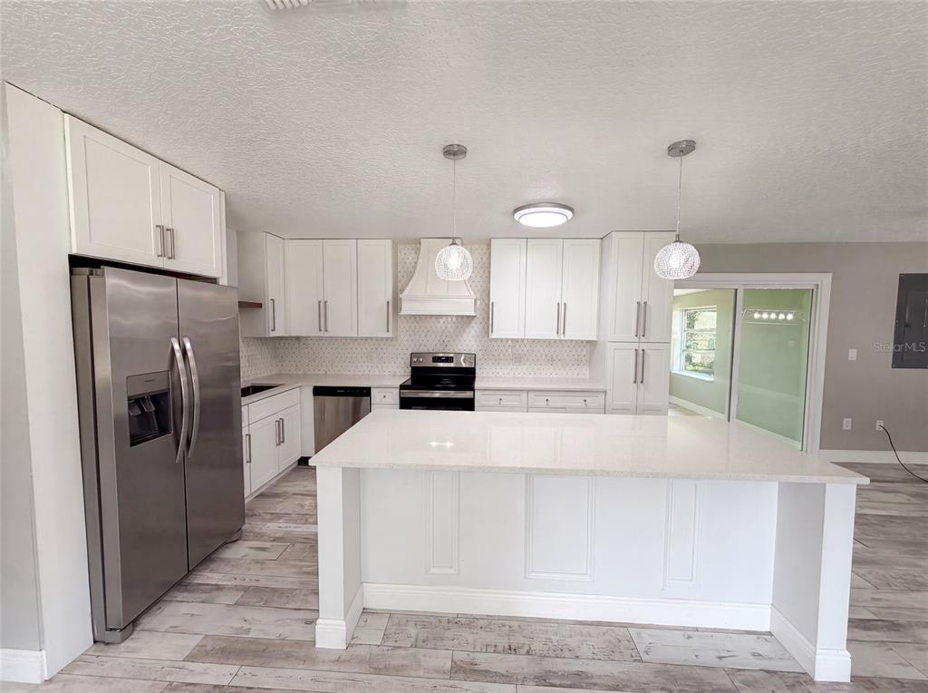 A modern kitchen features white cabinetry, stainless steel appliances, a large island, and wood-look flooring — 1044 E LOMBARDY DRIVE, DELTONA, FL