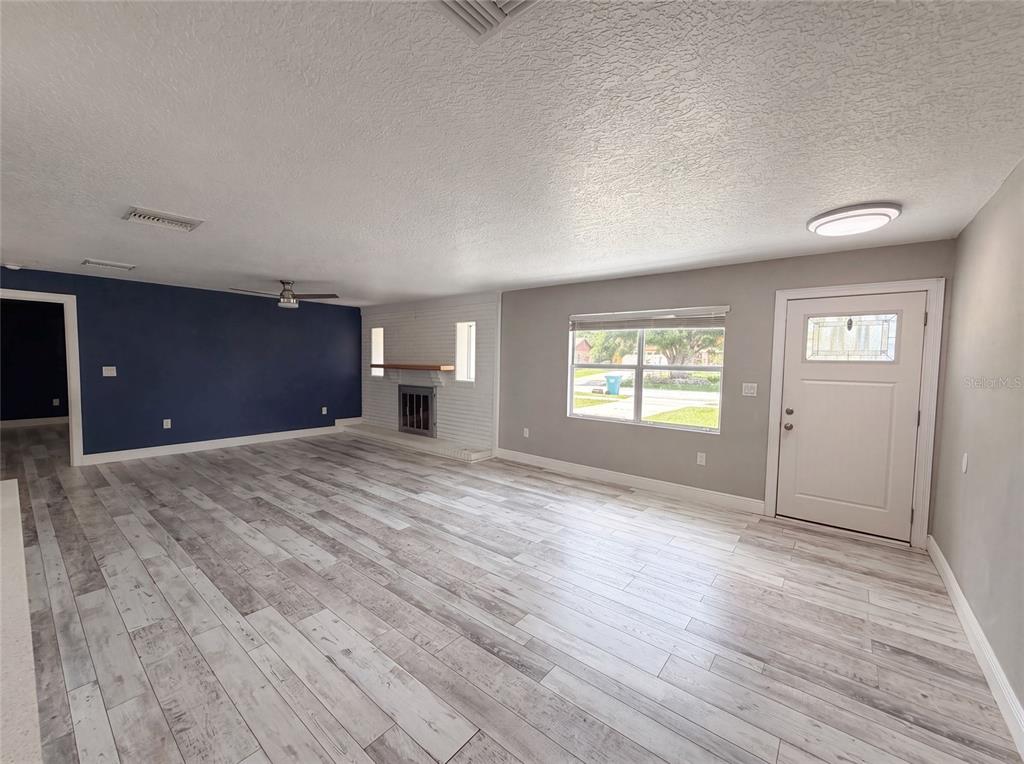 A living room features light wood-look flooring, a blue accent wall, and a white fireplace — 1044 E LOMBARDY DRIVE, DELTONA, FL