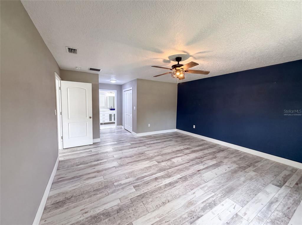 A bedroom with light wood-look flooring, a dark blue accent wall, and a ceiling fan — 1044 E LOMBARDY DRIVE, DELTONA, FL