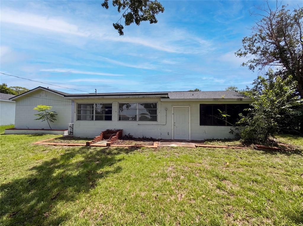 The exterior of a single-story house features white block walls, a shingled roof, and windows — 1044 E LOMBARDY DRIVE, DELTONA, FL