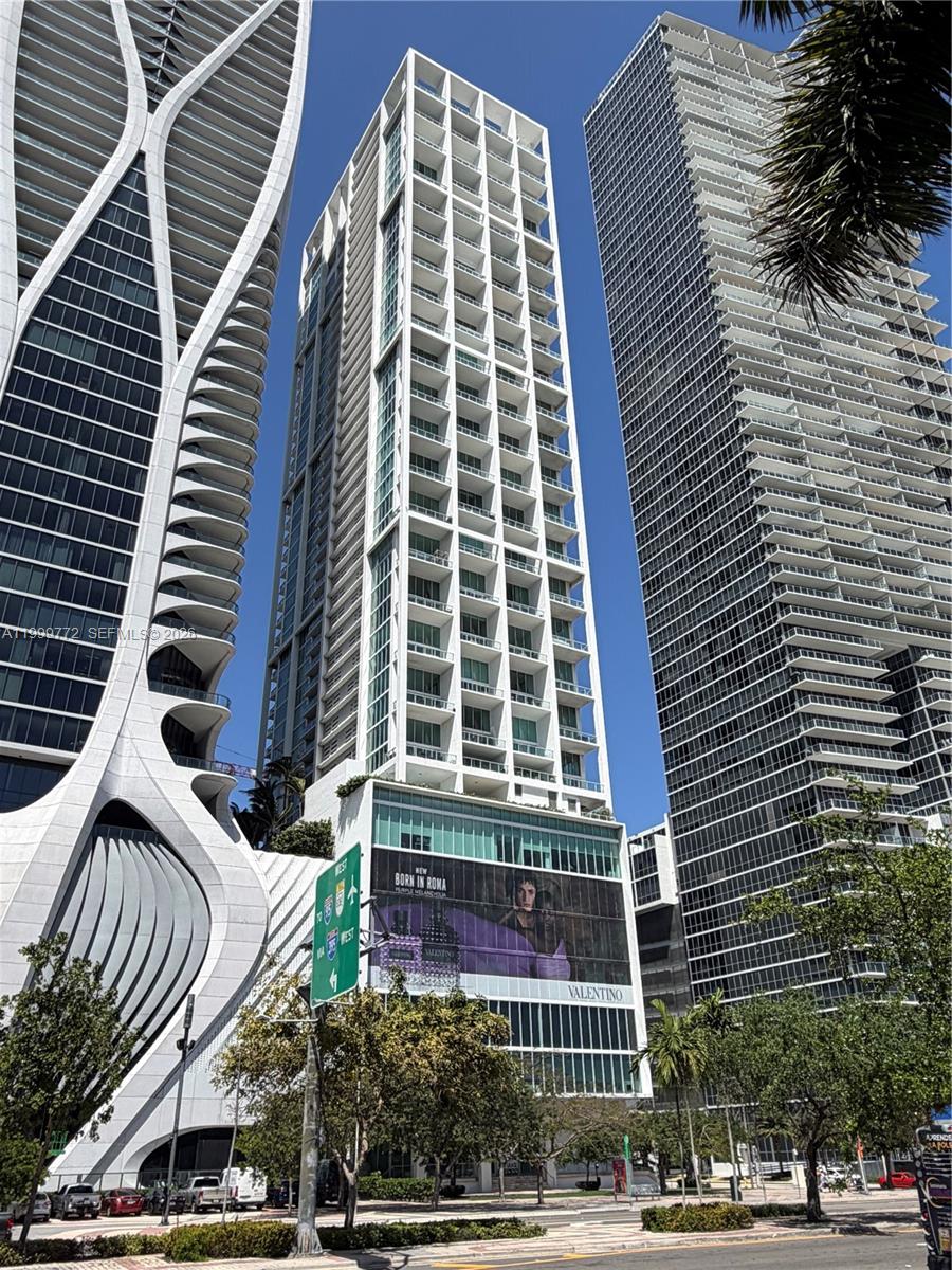 A low-angle view shows three modern high-rise buildings in an urban setting under a clear sky — 1040 Biscayne Blvd # 1001, Miami FL 33132, MIAMI, FL