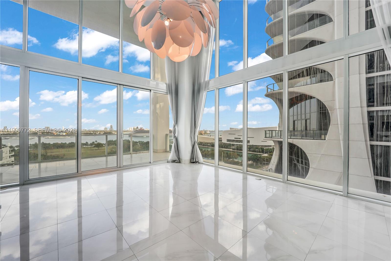 A bright, empty room features floor-to-ceiling windows, white tile floors, and a large modern chandelier — 1040 Biscayne Blvd # 1001, Miami FL 33132, MIAMI, FL
