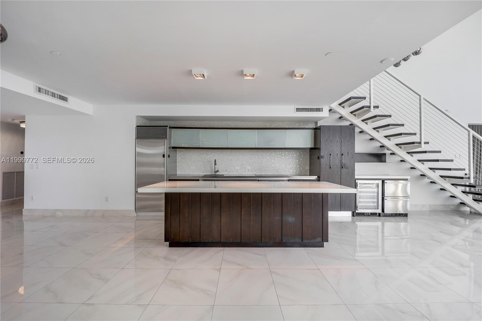 A modern kitchen features a dark wood island, white countertops, and a floating staircase — 1040 Biscayne Blvd # 1001, Miami FL 33132, MIAMI, FL
