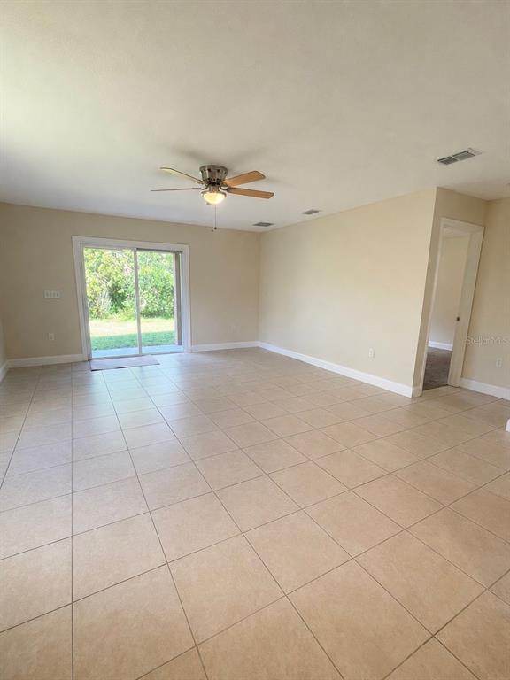 An empty room with beige tile floors, a ceiling fan, and sliding glass patio doors — 1002 MAYFAIR PLACE, KISSIMMEE, FL
