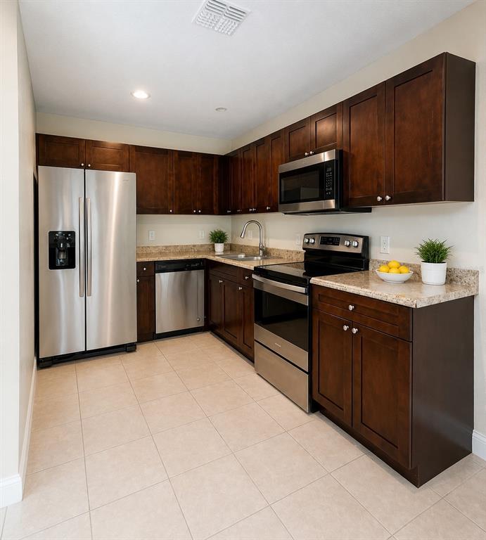 A kitchen with dark wood cabinets, stainless steel appliances, and light-colored granite countertops — 1002 MAYFAIR PLACE, KISSIMMEE, FL