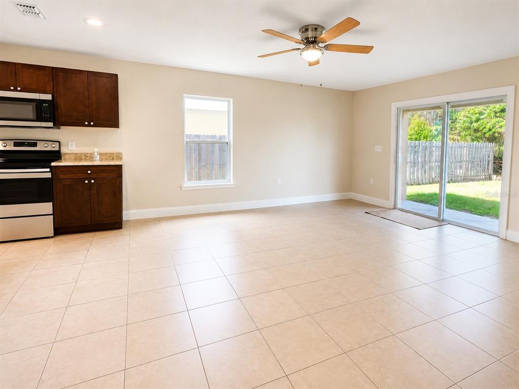A kitchen with dark wood cabinets and tile flooring opens to a backyard through sliding doors — 1002 MAYFAIR PLACE, KISSIMMEE, FL
