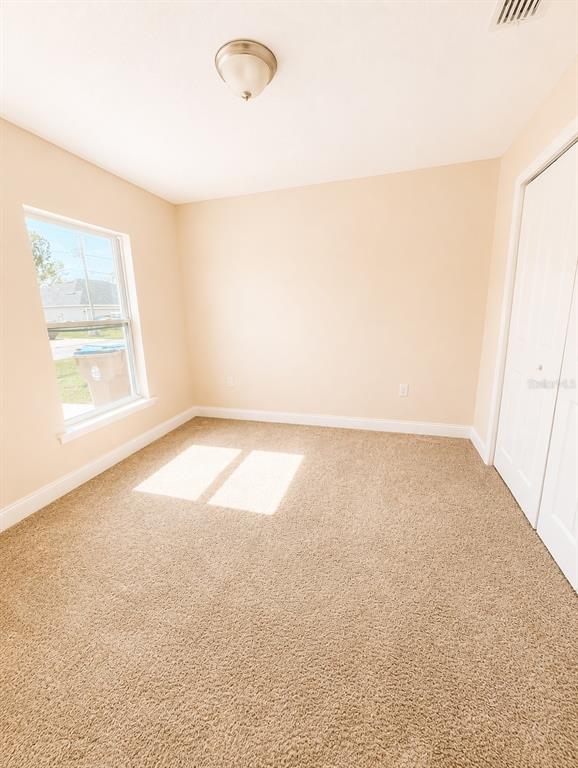 An empty bedroom features beige walls, tan carpeting, a window, and white closet doors — 1002 MAYFAIR PLACE, KISSIMMEE, FL