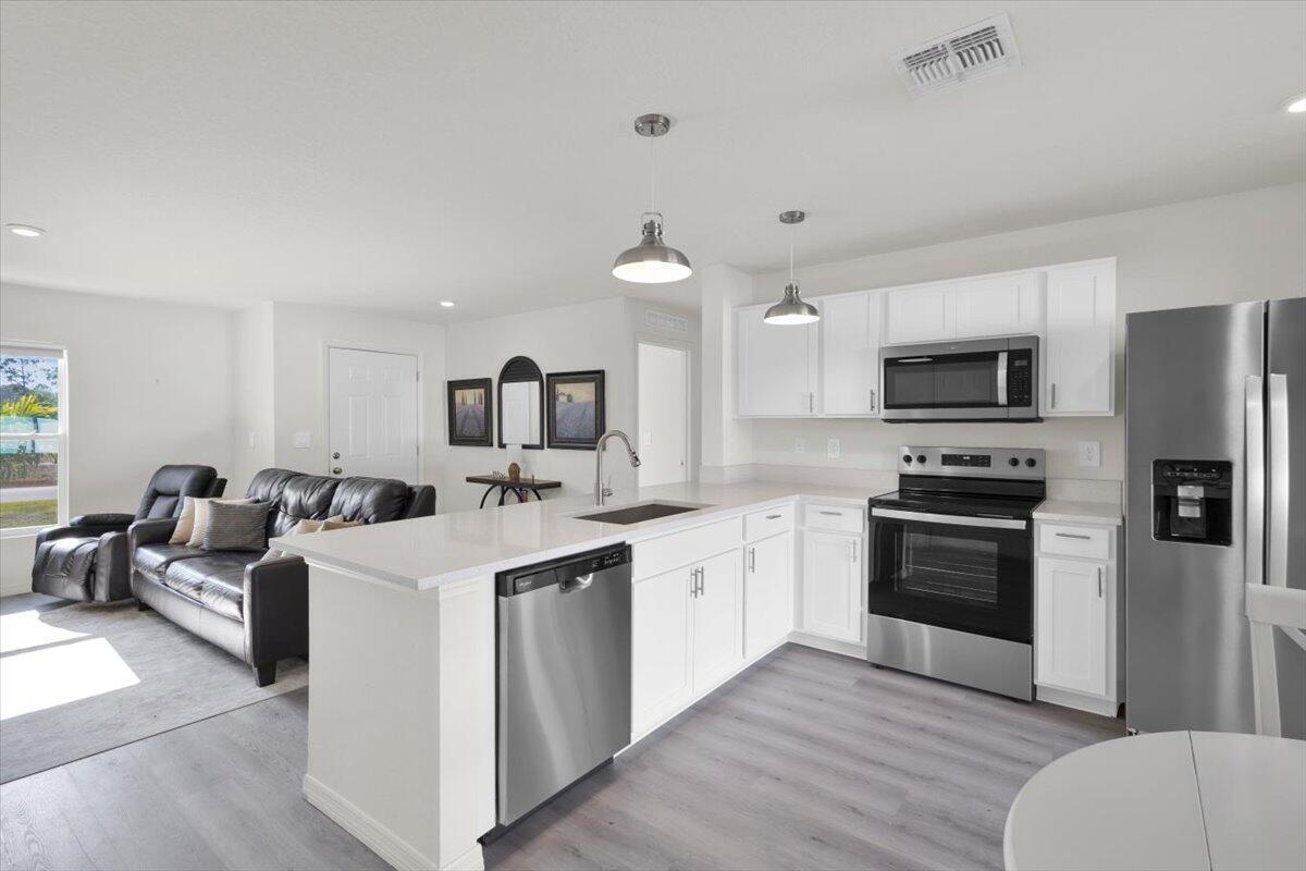 A kitchen with white cabinets and stainless steel appliances overlooks a living area with furniture — 3129 Wessel Avenue SE, Palm Bay FL 32909, PALM BAY, FL