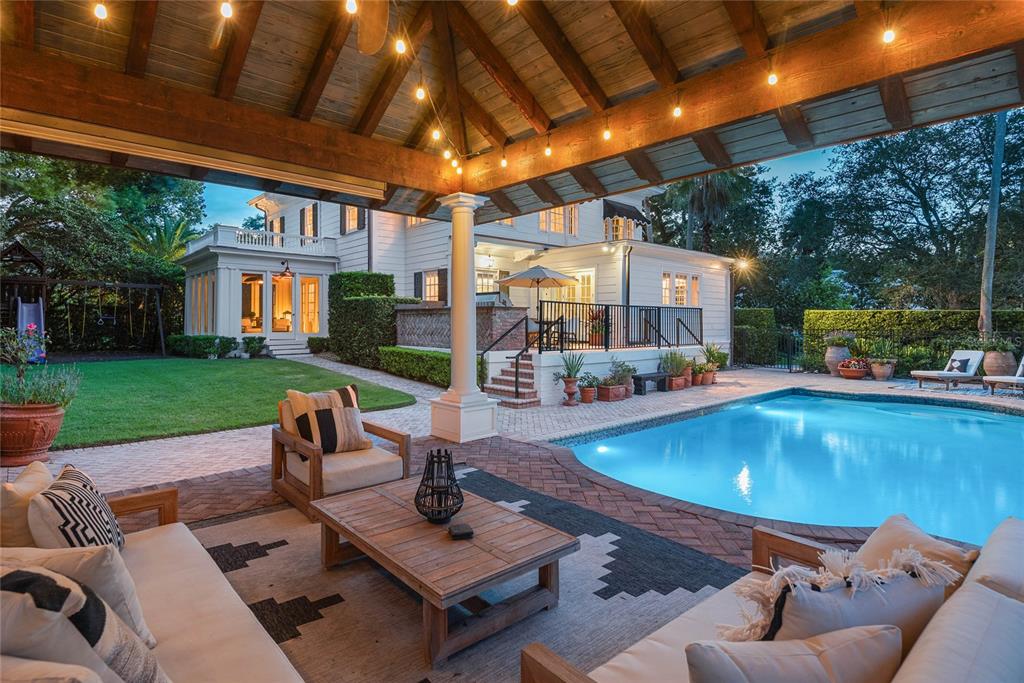 A covered patio with outdoor seating overlooks a swimming pool and a white house — 705 DELANEY AVENUE, ORLANDO, FL