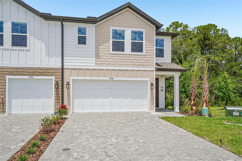 A two-story townhouse exterior features a paved driveway, two garage doors, and tan siding — 7524 DEER VALLEY CIRCLE, TAMPA, FL