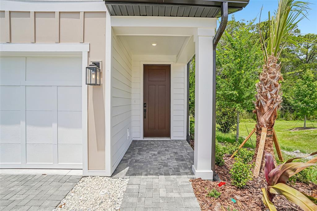 A brown front door is set within a covered entryway next to a white garage — 7524 DEER VALLEY CIRCLE, TAMPA, FL