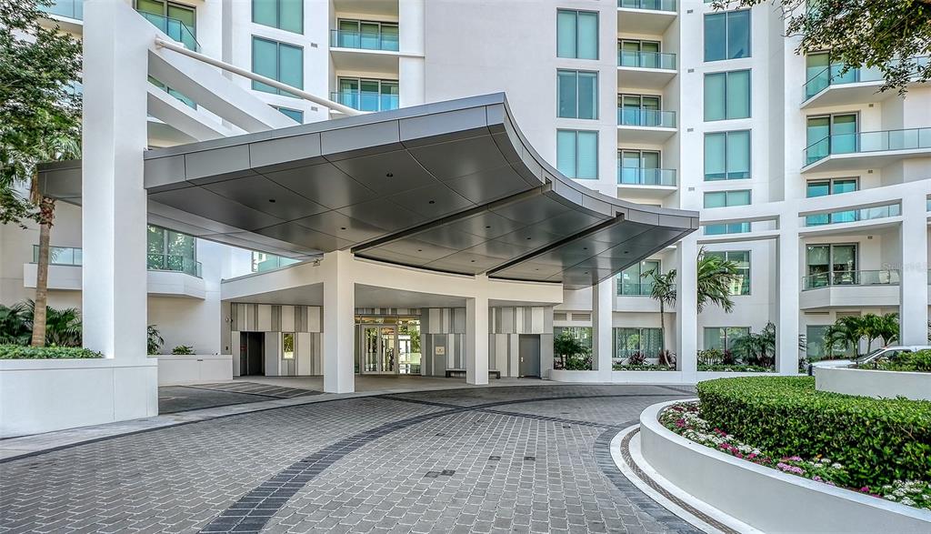 A modern apartment building features a large, curved metal porte-cochère over a paved driveway — 401 QUAY COMMONS UNIT 1004, SARASOTA, FL