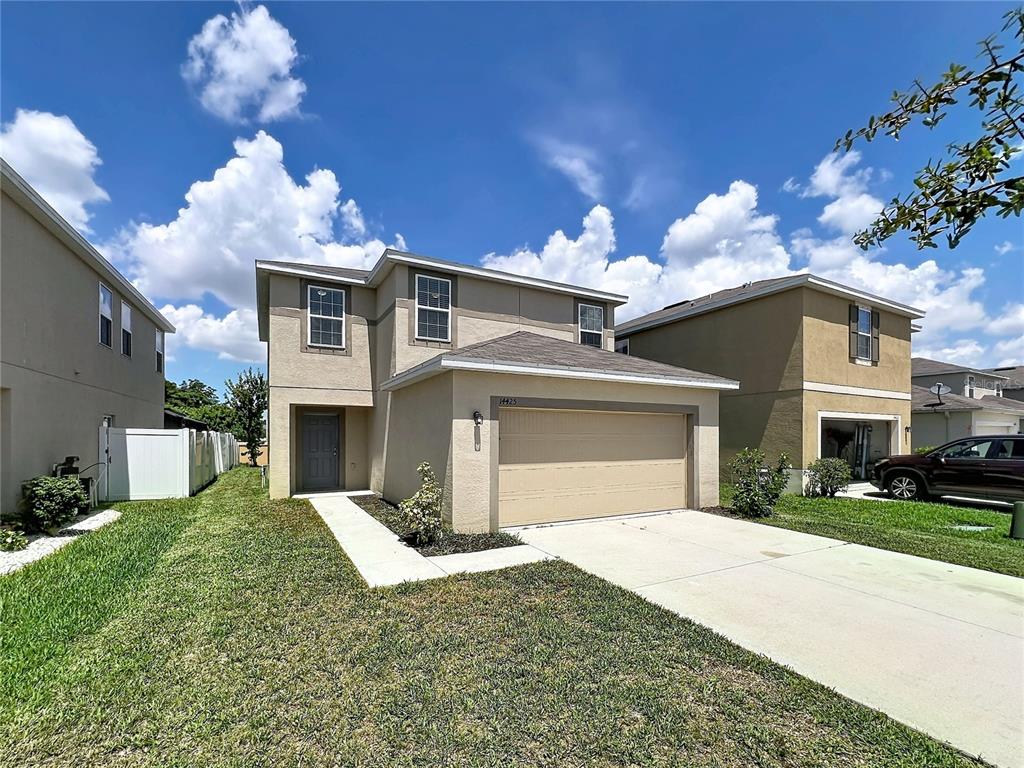 A two-story suburban house features a tan stucco exterior, a two-car garage, and a driveway — 14425 DUNROBIN DRIVE, WIMAUMA, FL