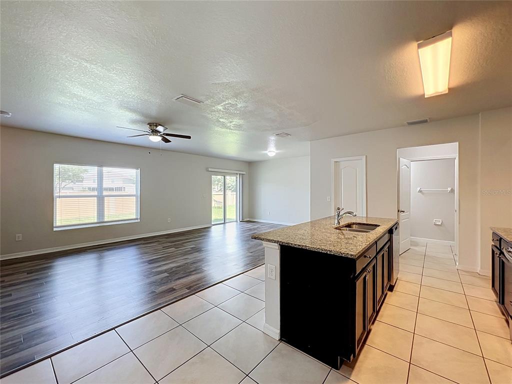An open-concept kitchen with a granite island overlooks a living area with wood-look flooring — 14425 DUNROBIN DRIVE, WIMAUMA, FL