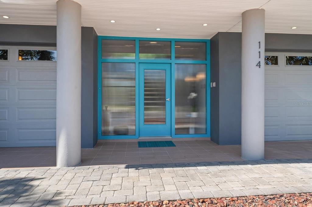 A teal front door with glass panels is flanked by two columns and garage doors — 114 13TH STREET, BELLEAIR BEACH, FL